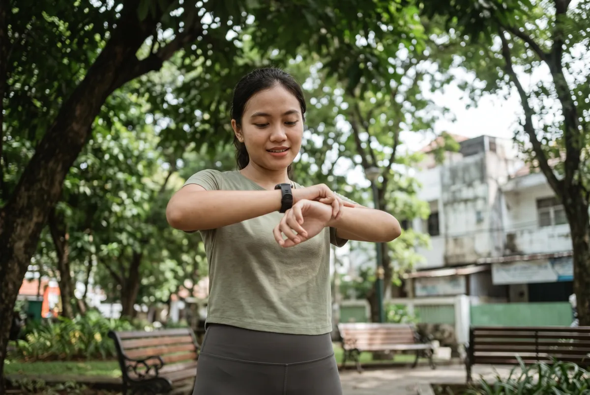 Indonesian beginner runner reviewing a sports watch after an easy run in a leafy urban park, candid relaxed expression, 